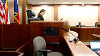 A photo of a judge in a courtroom with an empty witness chair to her right.