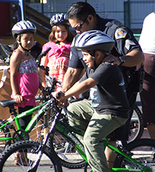 Police officer helps young boy ride a bike.