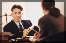 Photo of a an expert witness being questioned by a female attorney on a courtroom stand. 